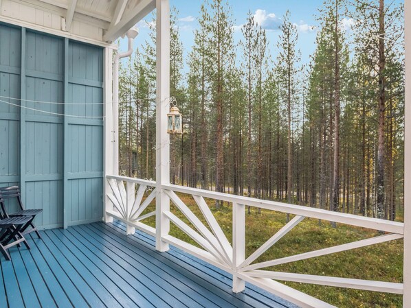 A covered porch with a view of a forest.