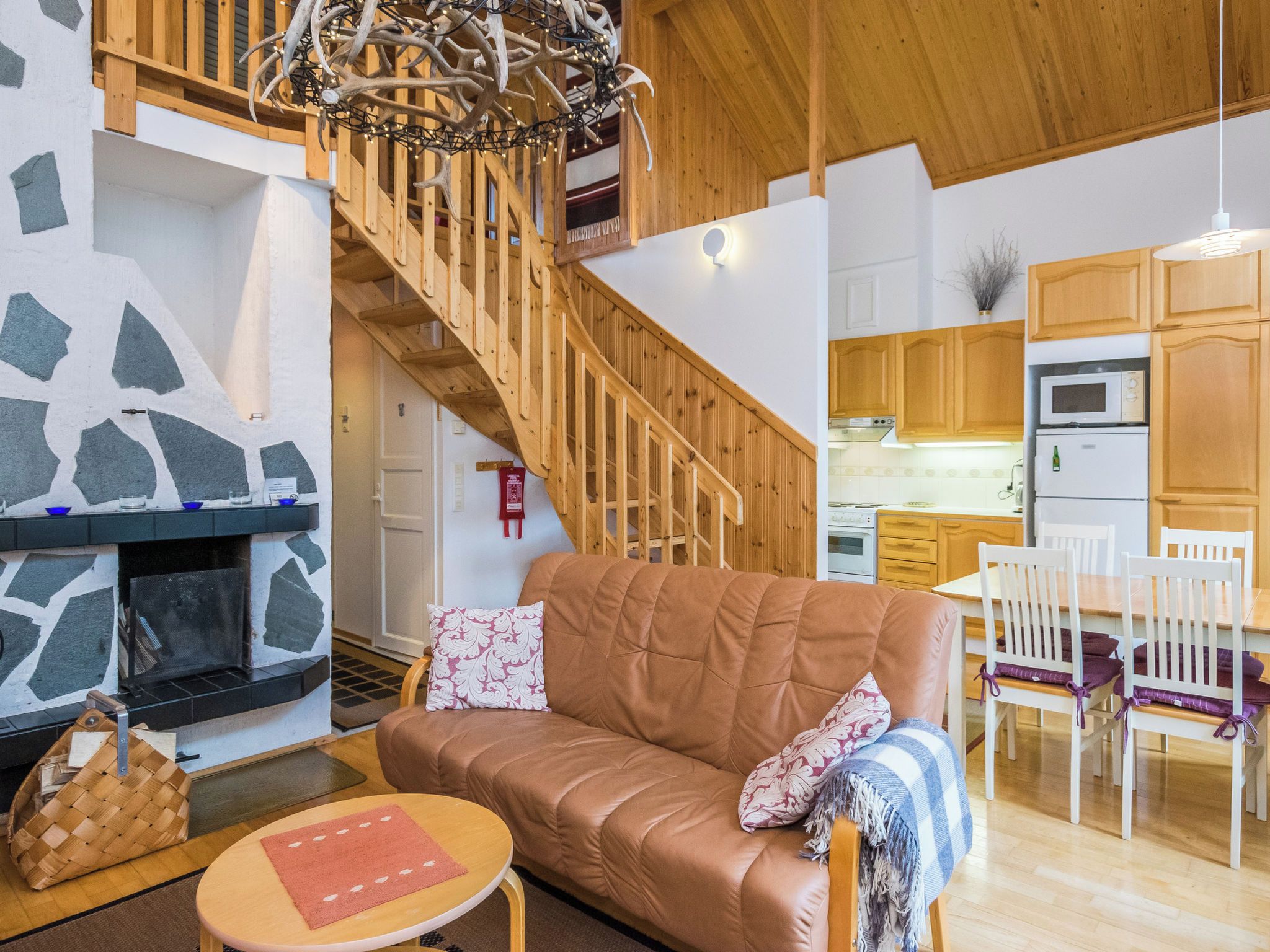 A cozy living room with a fireplace, a sofa, a dining table with chairs, and a kitchen area with wooden cabinets and appliances.