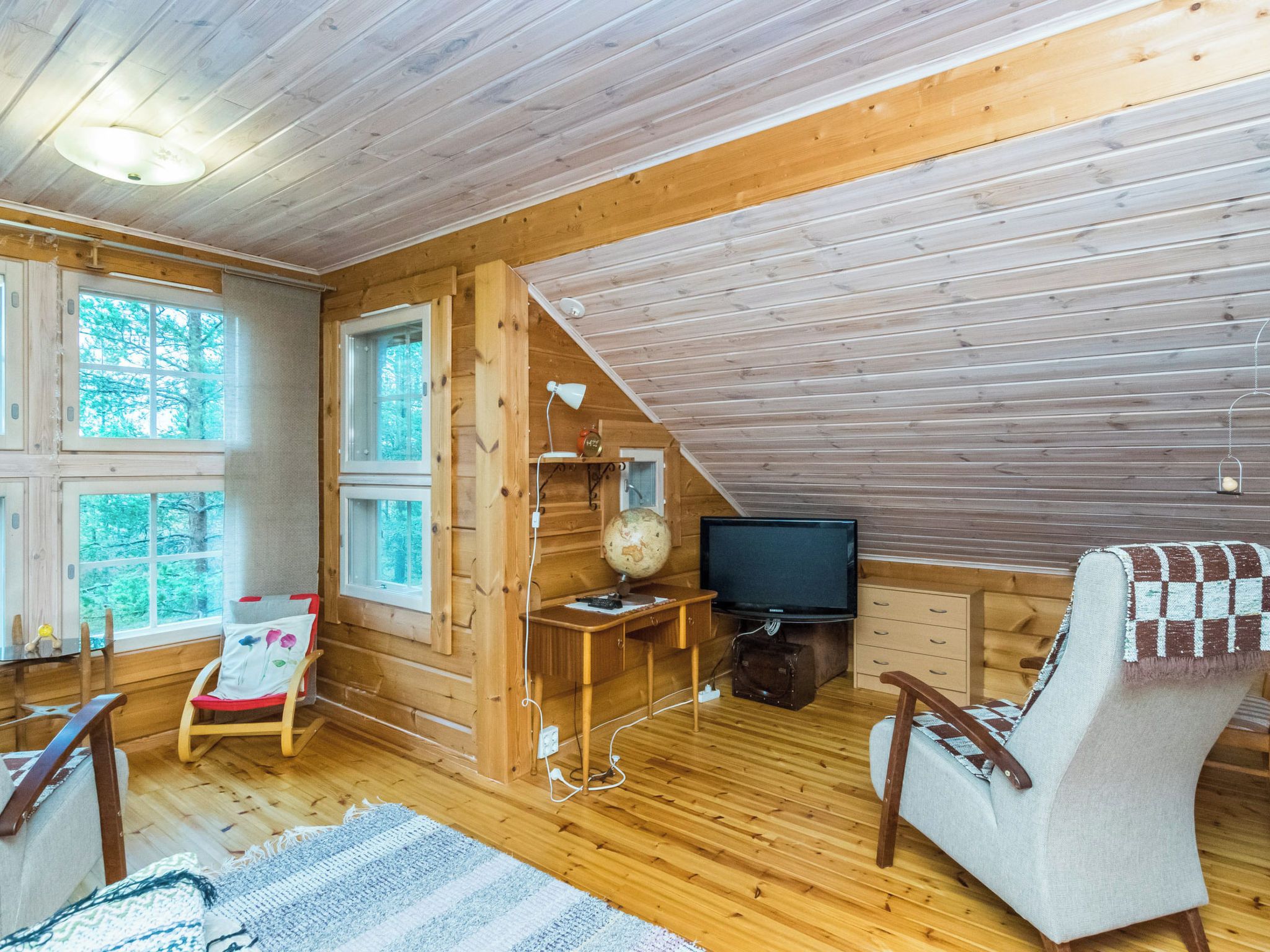 A cozy cabin interior with a wooden floor, a television, a globe, and a rocking chair.