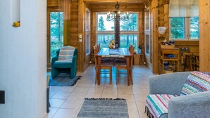 L’intérieur d’un chalet accueillant, avec une table à manger en bois, des chaises, un lustre et une horloge au mur.