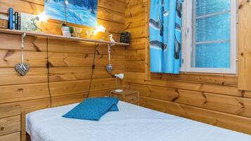 Een houten kamer met een bed, een plank met boeken en decoratieve spullen, een schilderij en een raam met gordijnen.