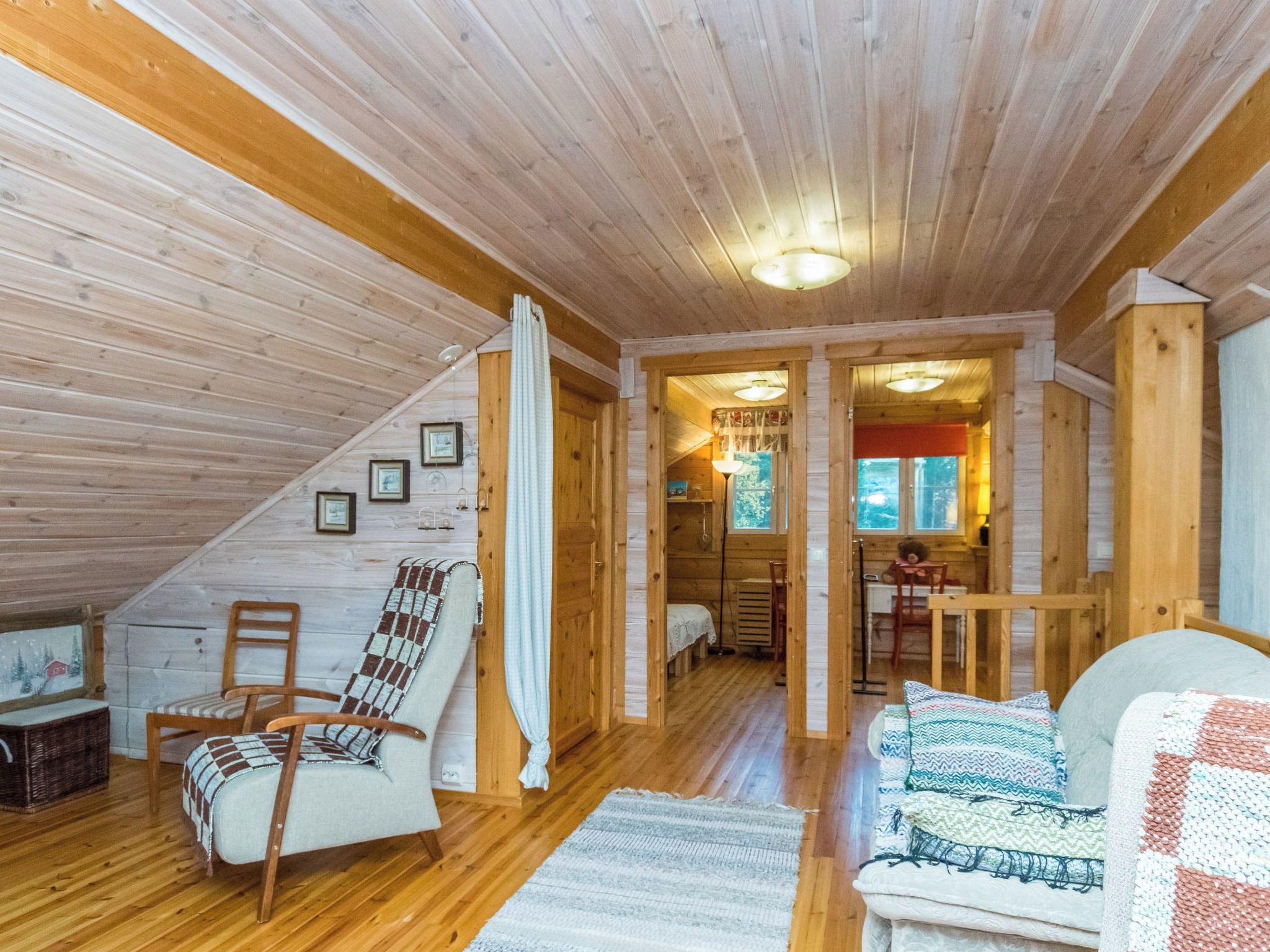 Interior acogedor de una cabaña de madera con un altillo, comedor y sala de estar amueblada con un sofá, sillas y una alfombra estampada.