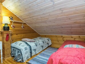 A cozy attic bedroom with a sloped ceiling, a single bed with patterned bedding, a small table with a lamp, and a shelf with decorative items.