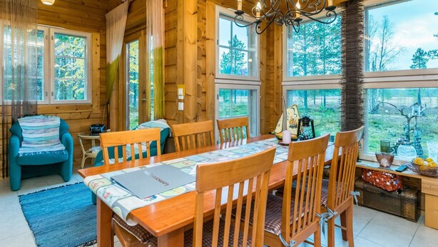 Une cabane en bois dotée d’un coin repas, de grandes fenêtres et d’un lustre.