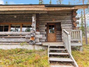 A rustic log cabin with a wooden door, a small porch, and a staircase leading to the entrance.