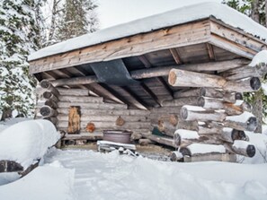 Una cabaña de troncos con techo y paredes cubiertas de nieve, rodeada de ventiscas.