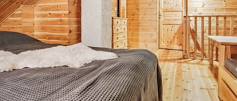 Quarto de cabana de madeira com cama, cômoda e uma pequena mesa.