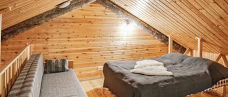 A cozy attic bedroom with a wooden sloped ceiling, a single bed, and a bench with cushions.