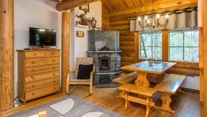 A cozy log cabin interior with a stone fireplace, wooden furniture, and a television on a dresser.