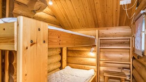 A wooden cabin interior with a bunk bed, a small desk, and a shelf with books.