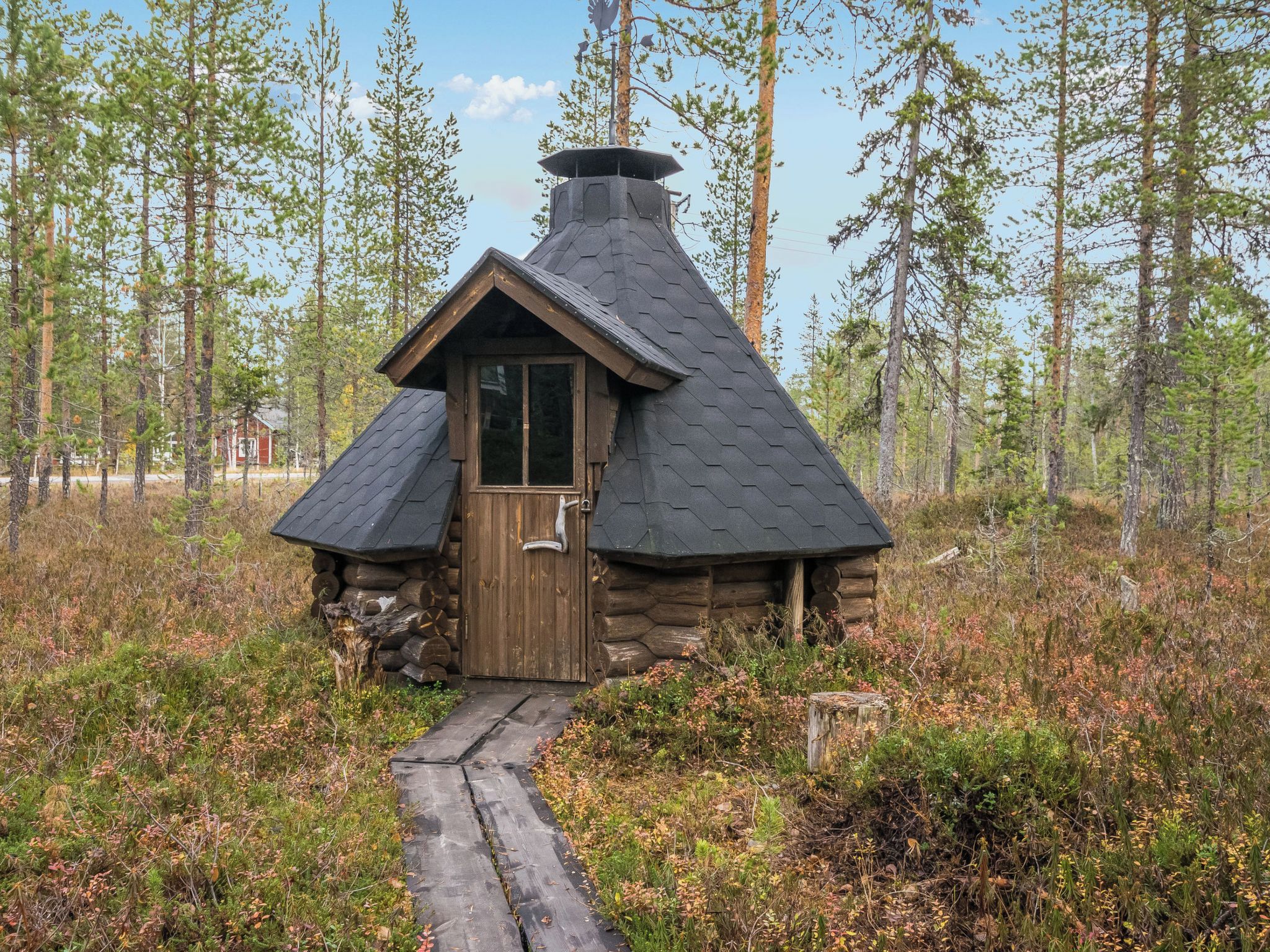 Hirsimökki, jossa on puuovi ja savupiippu, ja jonka ympärillä on metsä.