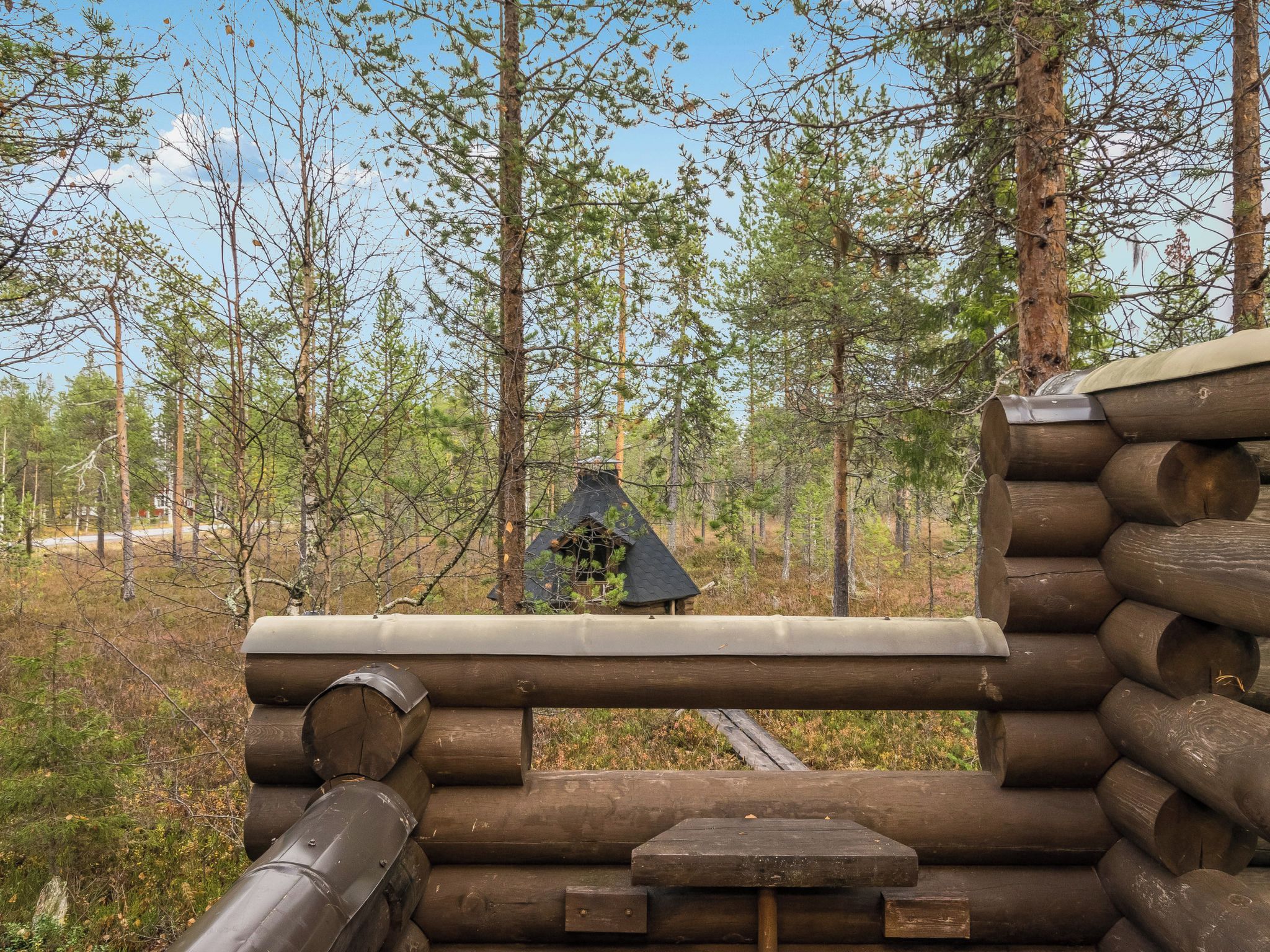 Una cabaña de troncos con techo de metal, rodeada de un bosque.