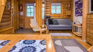 A log cabin interior with a sofa, wooden chairs, a table, and a television.