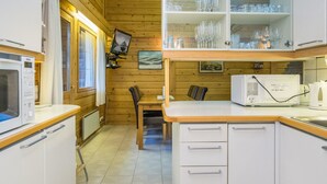 A compact kitchen with wooden walls, a microwave, a refrigerator, and a glass cabinet with dishes.