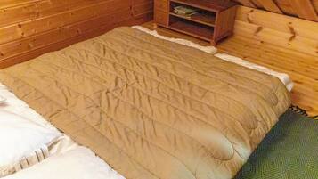 Een houten kamer met een bed, een klein houten kistje en een vloerkleed met een groen patroon.