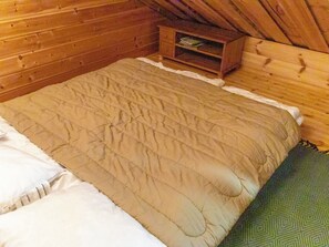 A wooden cabin room with a bed, a small wooden chest, and a green patterned rug. - Antura b by Interhome (Pelkosenniemi)