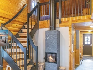 Un interior de madera con chimenea, una escalera y una puerta con un ventanal en forma de corazón.