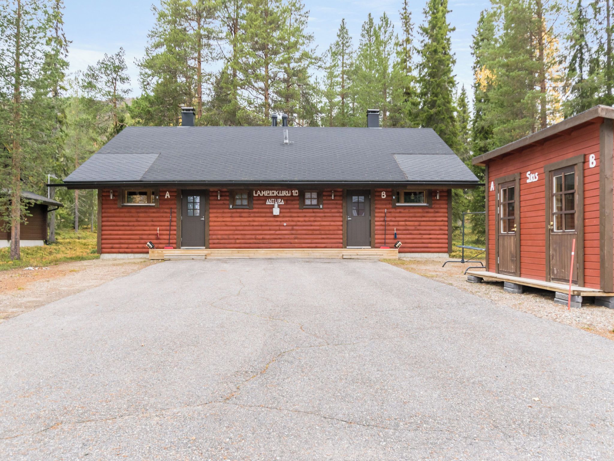 A red log cabin with a black roof, labeled 'LAMPIKKURU 10 ANTURA,' and a smaller adjacent building marked '8.'