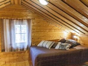 A cozy bedroom with a wooden ceiling, a bed with multiple pillows, and a window with curtains.