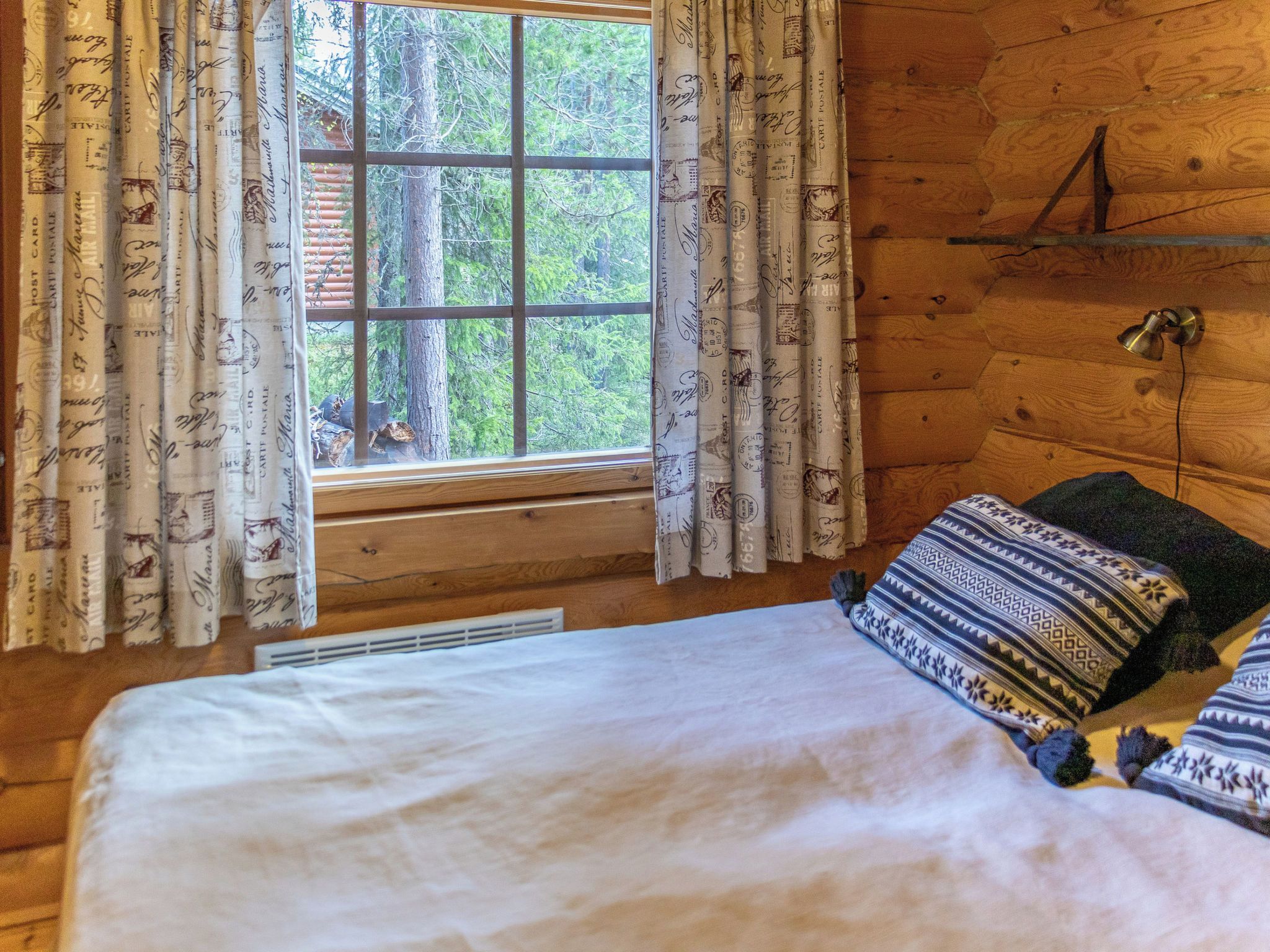 Een houten kamer met een bed, een raam met gordijnen en een wandlamp.