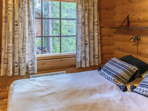 A wooden cabin room with a bed, a window with curtains, and a wall-mounted lamp. - Antura b by Interhome (Pelkosenniemi)