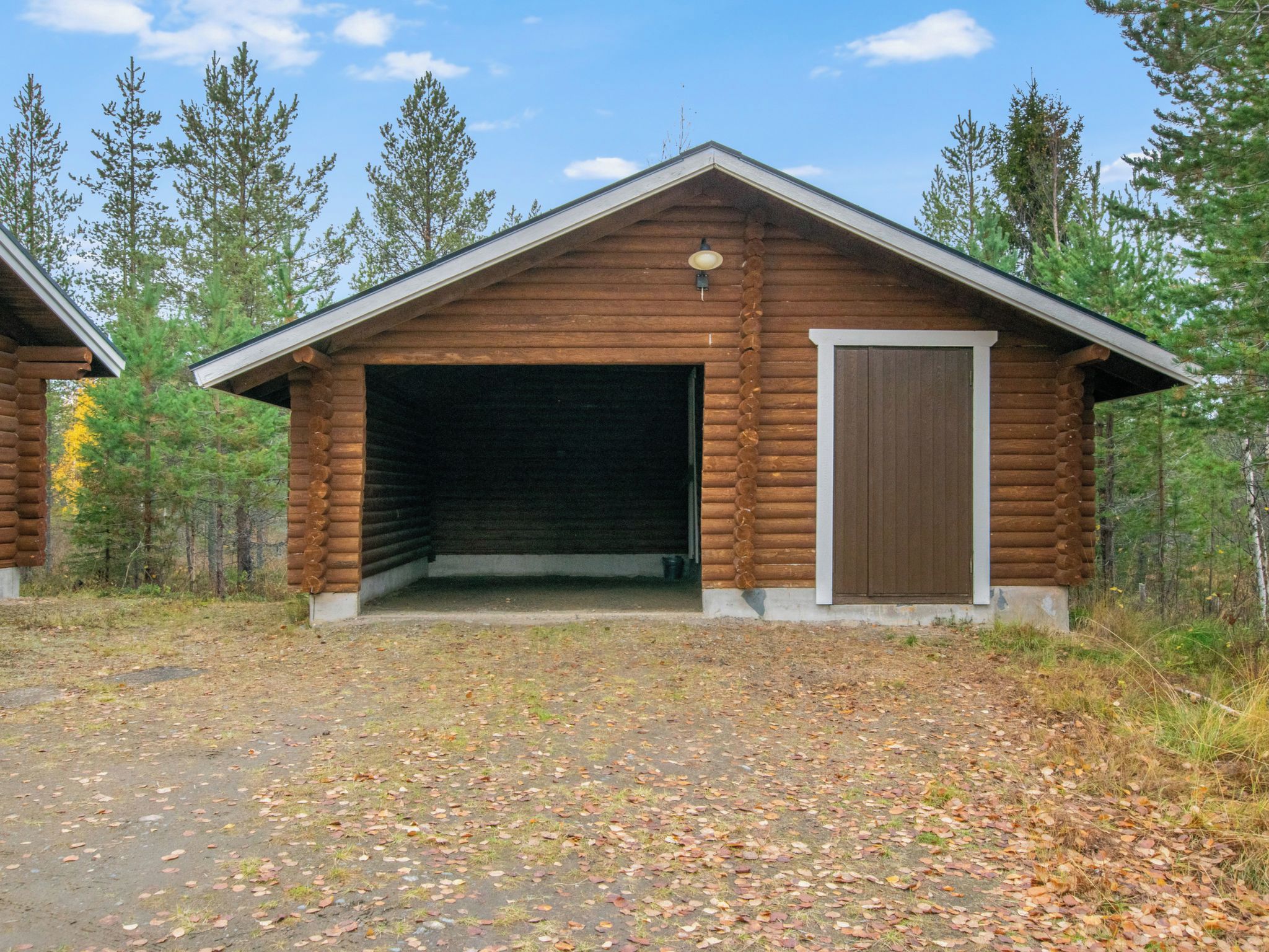 Suuri autotallioven omaava hirsihökkelö, jonka ympärillä on metsää.