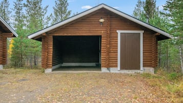 Suuri autotallioven omaava hirsihökkelö, jonka ympärillä on metsää.