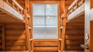 A wooden cabin with bunk beds, a wooden staircase, and a window with blinds.