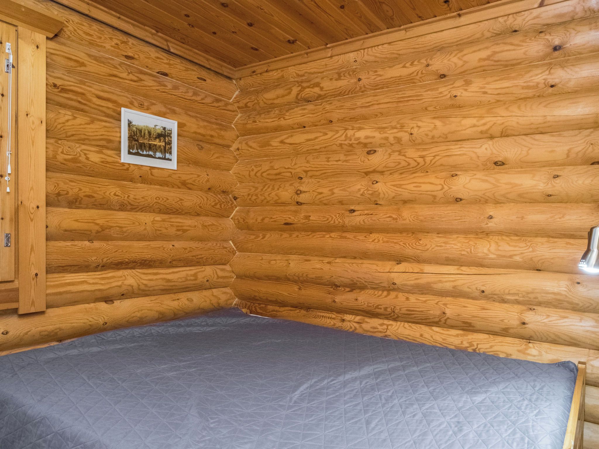 Interior d'una cabana de fusta amb un llit, una fotografia emmarcada a la paret i una porta de fusta.