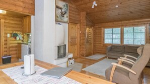 A cozy cabin interior with a fireplace, wooden walls, a sofa, and a dining area.
