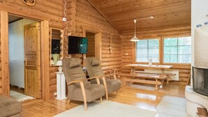 A log cabin interior with a wooden floor, a fireplace, a television, and a dining area.