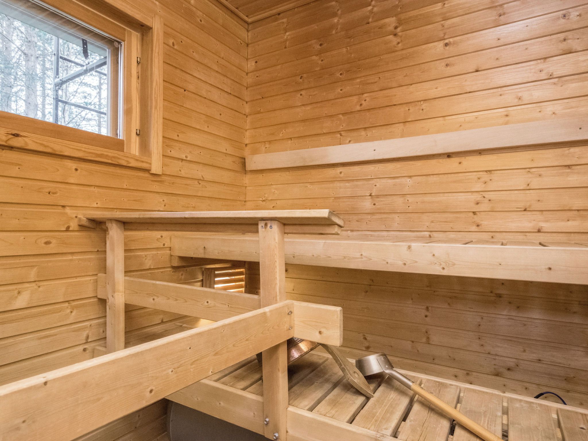 Interior de una cabaña de madera con una ventana, un banco de madera y una pala.
