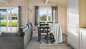 A cozy cabin interior with a sofa, dining table, and a view of the outdoors. - Chestnut Lodge - Pet Friendly - Free Parking & WiFi (Exeter)