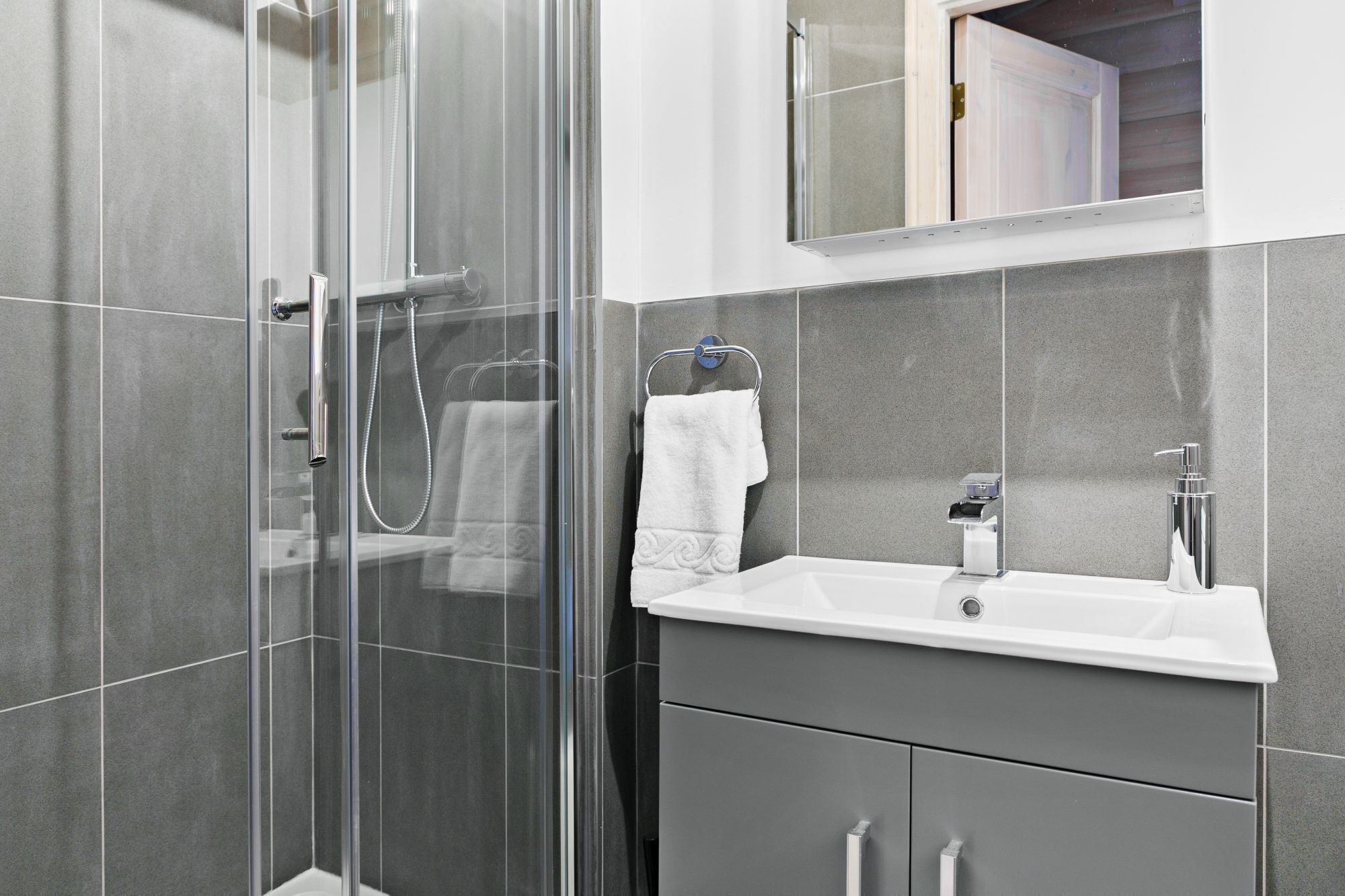 Une salle de bain moderne avec une douche à parois de verre, un lavabo blanc et un miroir au-dessus du lavabo.