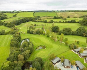 An aerial view of a golf course with a clubhouse, a pond, and surrounding fields. - Chestnut Lodge - Hot Tub - Pet Friendly - Free Parking & WiFi - Golf Course (Exeter)