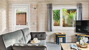 A cozy living room with a grey sofa, a small wooden table, a TV, and a window with curtains. - Chestnut Lodge - Pet Friendly - Free Parking & WiFi (Exeter)