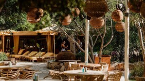 An outdoor seating area with wicker furniture and hanging lanterns, surrounded by greenery.