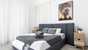 A modern bedroom with a large bed, grey bedding, a wooden nightstand, and a framed artwork on the wall.