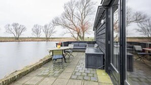 Eine Terrasse mit Tisch und Stühlen, eine integrierte Bank und Blick auf ein Gewässer.