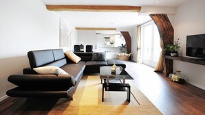 Ein modernes Wohnzimmer mit einer schwarzen Couch, einem Couchtisch und einem Fernseher auf einem Holzboden.