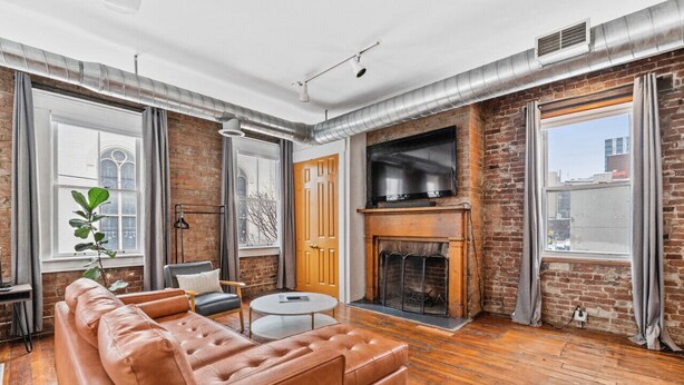 Un salon moderne avec un mur en briques, une cheminée, un canapé en cuir et un grand téléviseur.