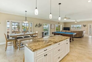 A spacious kitchen with a central island, dining area, and a pool table.