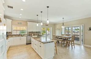A spacious kitchen with white cabinets, a granite countertop, and pendant lighting.
