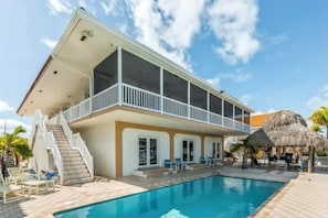 A two-story house with a balcony, a swimming pool, and a thatched-roof structure.