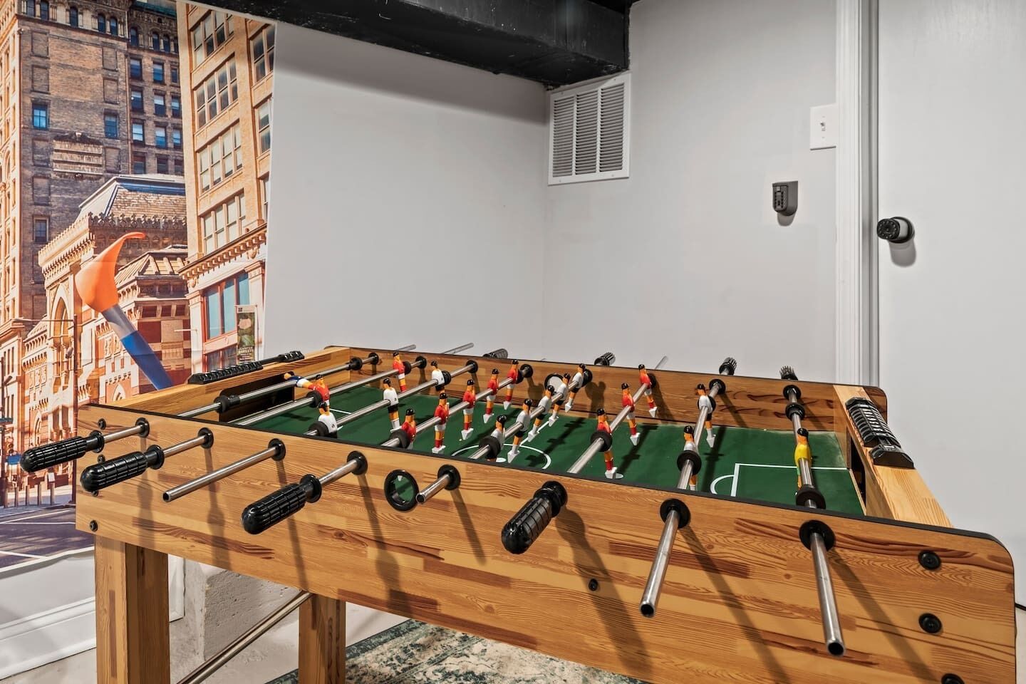 Una taula de futbolí a una habitació amb un mural que representa un paisatge urbà a la paret.