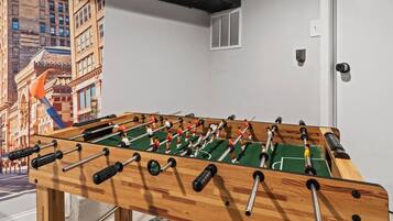 Una taula de futbolí a una habitació amb un mural que representa un paisatge urbà a la paret.