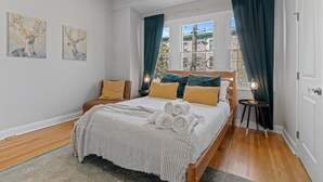 A modern bedroom with a large bed, two side chairs, a small table, and artwork on the walls. - Spacious 3BR Near Art Museum | Patio | Gameroom (Philadelphia)