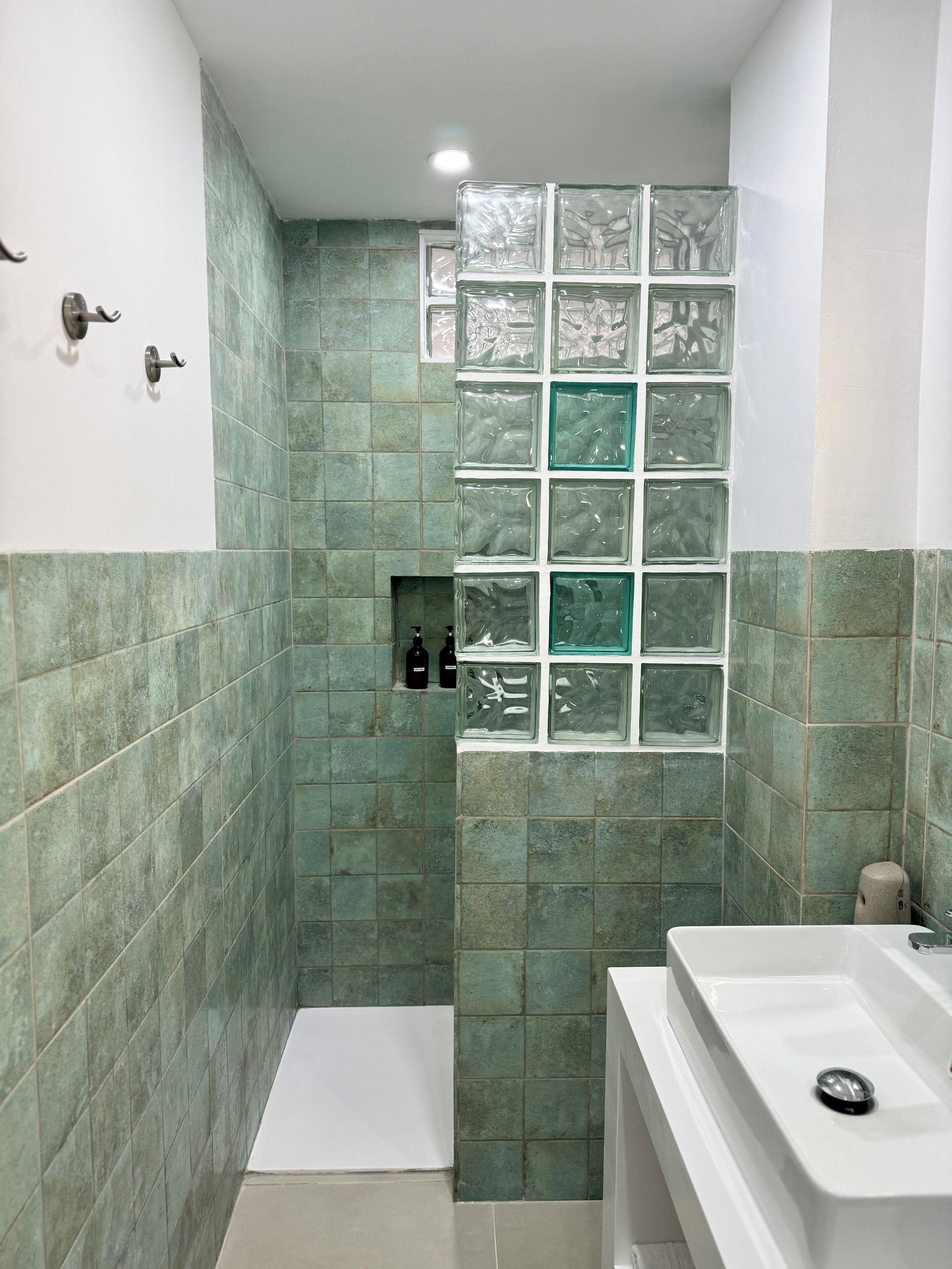 Un baño con baldosas verdes, cabina de ducha de vidrio, lavamanos blanco y toallero.