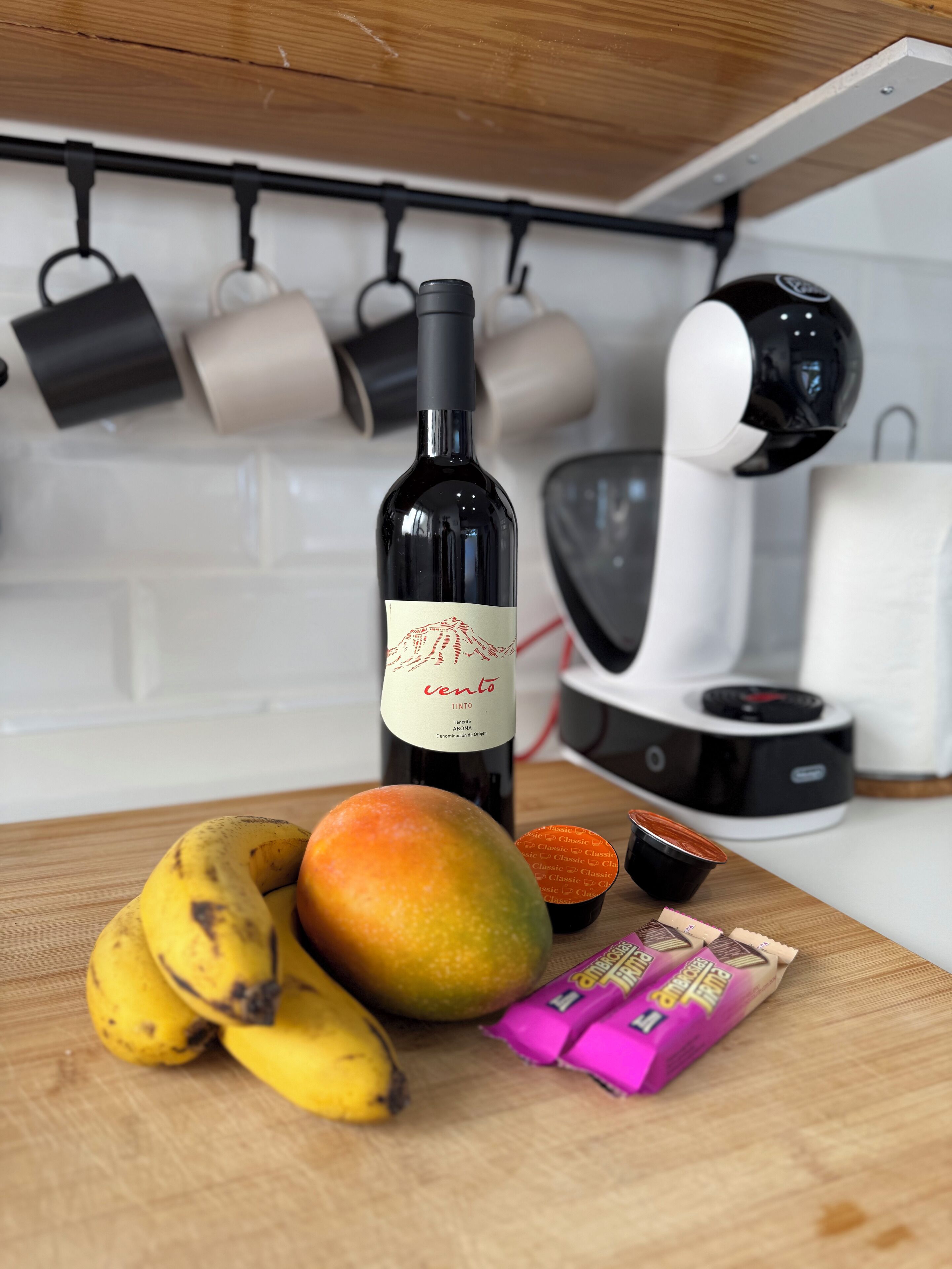 Een aanrecht met een fles wijn, een mango, bananen en chocoladerepen.