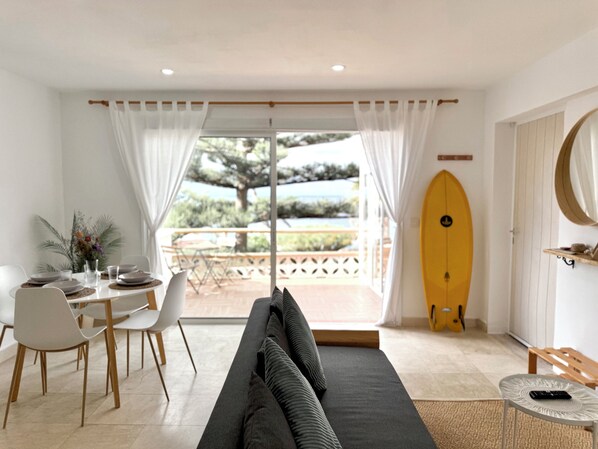 A modern living room with a sofa, dining table, chairs, and a surfboard. - Apartment with a terrace overlooking the ocean and the sunset (Bajamar)